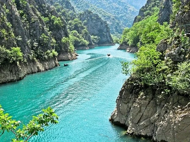 A motorboat trails a wake through the deep gorge of Matka Canyon.