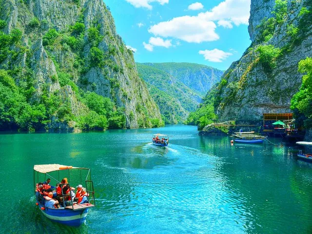 A scenic view of Matka Canyon with boats on emerald green water.
