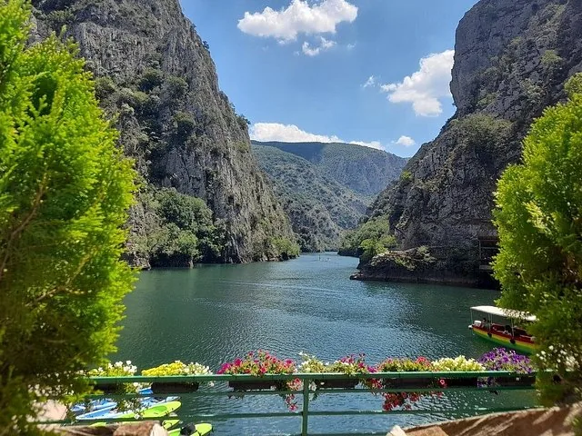 A vibrant view of Matka Canyon framed by green foliage and colorful flowers.