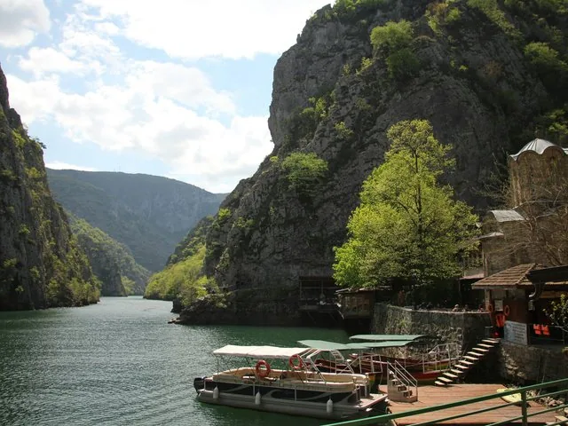 A picturesque view of Matka Canyon showing boats docked near a stone monastery.