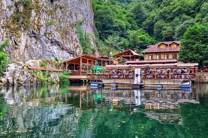 A waterside restaurant with floral decorations nestles against the rocky cliffs of Matka Canyon.