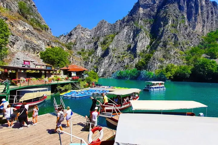 Visitors gather at the bustling dock of Matka Canyon surrounded by dramatic cliffs.