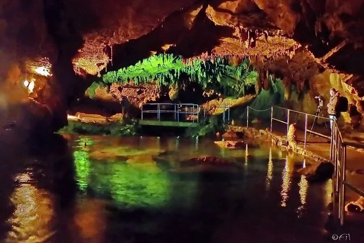 Illuminated rock formations and a tranquil underground pool inside Vrelo Cave.