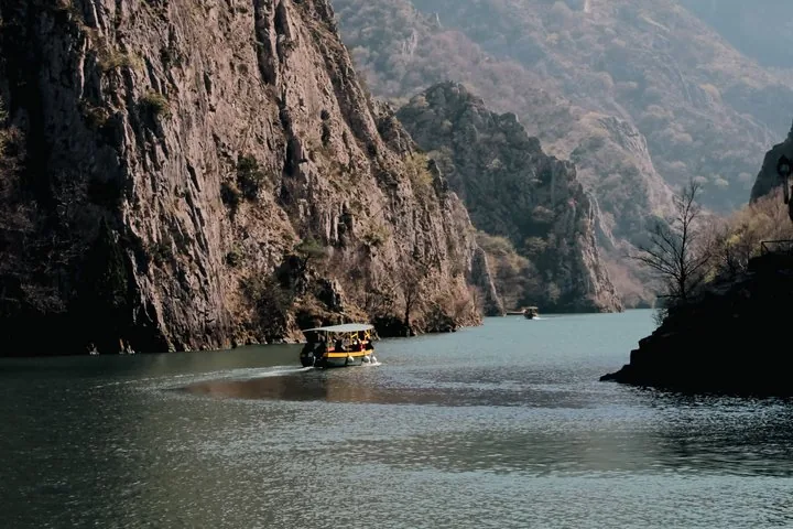 A small boat navigates the calm waters between the steep, rugged cliffs of Matka Canyon.