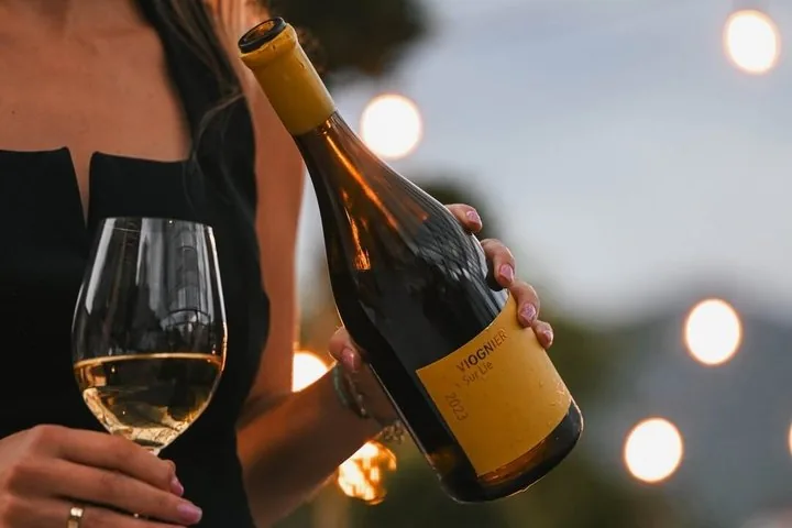 A person holding a glass of white wine and a bottle of Viognier Sur Lie.