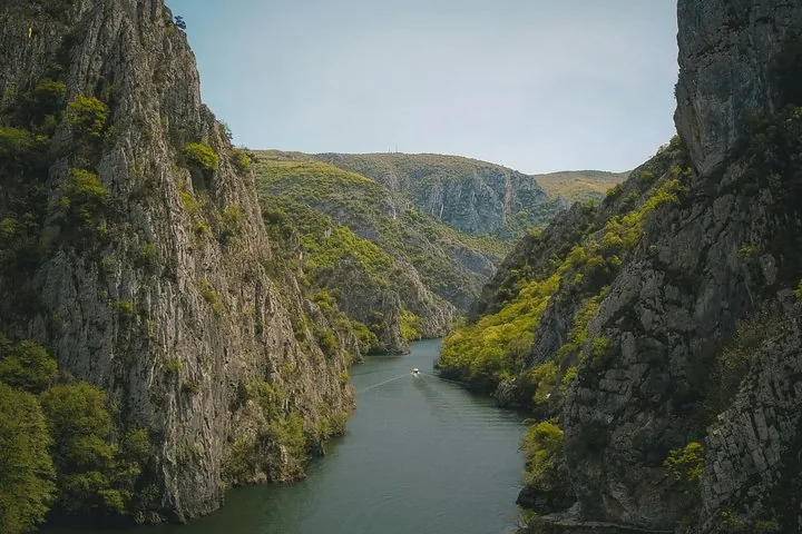 A solitary boat travels through the imposing, rocky landscape of Matka Canyon.